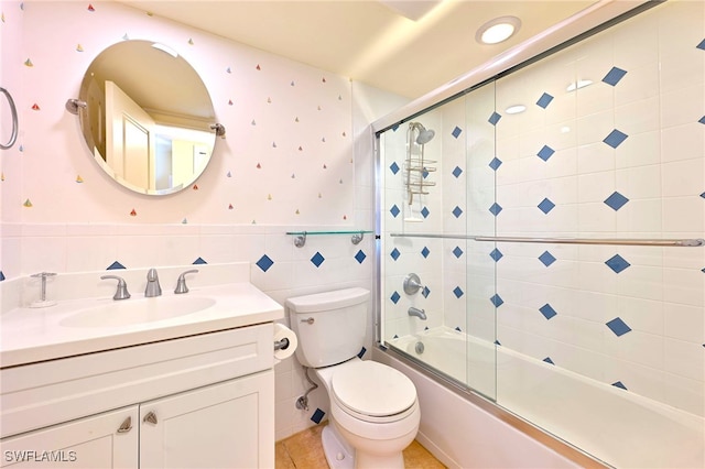 full bathroom with tile walls, bath / shower combo with glass door, vanity, tile patterned floors, and toilet