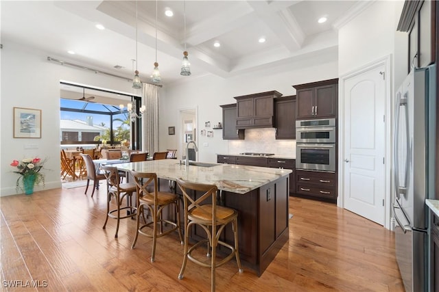 kitchen with sink, hanging light fixtures, a center island with sink, appliances with stainless steel finishes, and light stone countertops