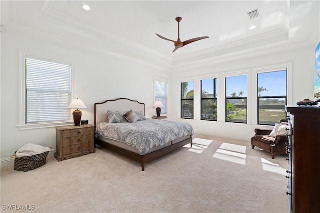 carpeted bedroom with multiple windows, ornamental molding, ceiling fan, and a tray ceiling