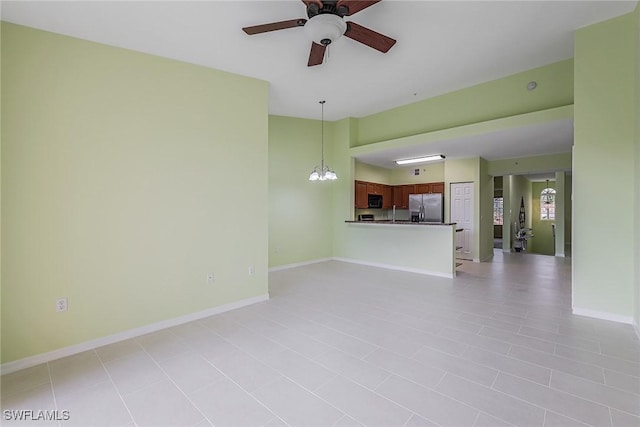 unfurnished living room featuring ceiling fan, a chandelier, and baseboards
