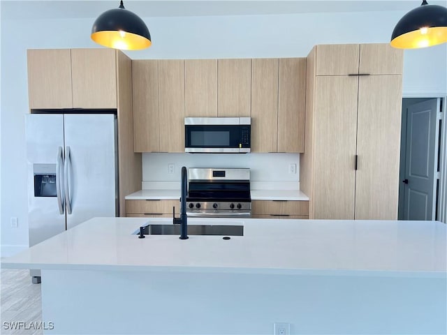 kitchen with pendant lighting, sink, a kitchen island with sink, stainless steel appliances, and light brown cabinets