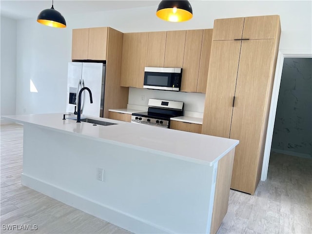 kitchen featuring sink, stainless steel appliances, a center island with sink, decorative light fixtures, and light wood-type flooring