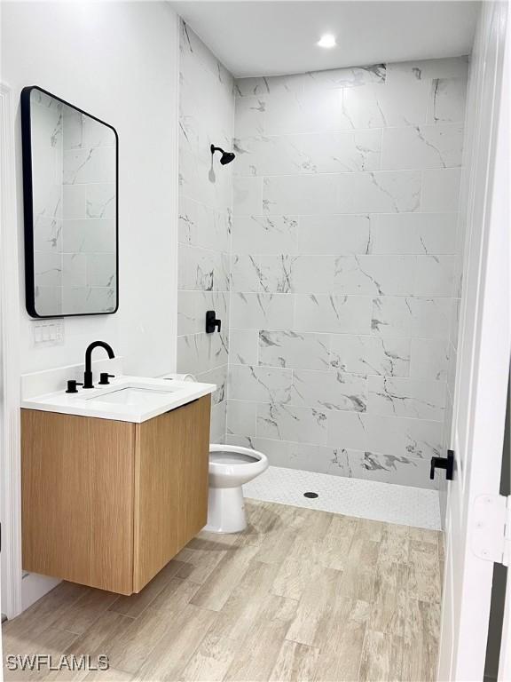 bathroom featuring vanity, tiled shower, hardwood / wood-style floors, and toilet