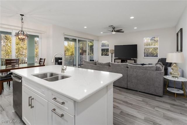 kitchen featuring ceiling fan with notable chandelier, pendant lighting, white cabinetry, an island with sink, and sink