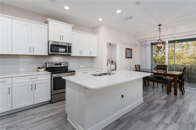 kitchen featuring hanging light fixtures, backsplash, white cabinets, and appliances with stainless steel finishes