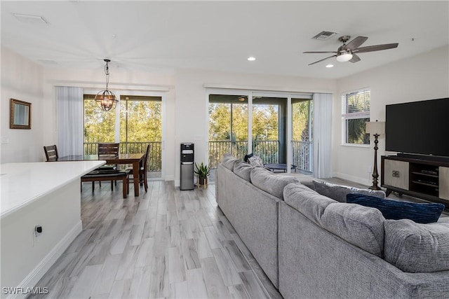 living room with ceiling fan with notable chandelier and light hardwood / wood-style flooring