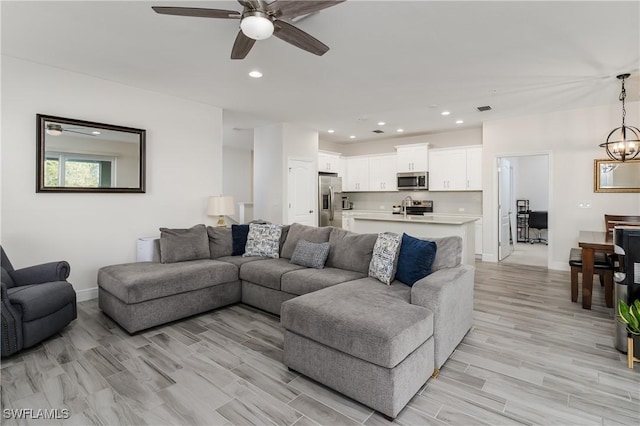 living room featuring ceiling fan with notable chandelier and light wood-type flooring