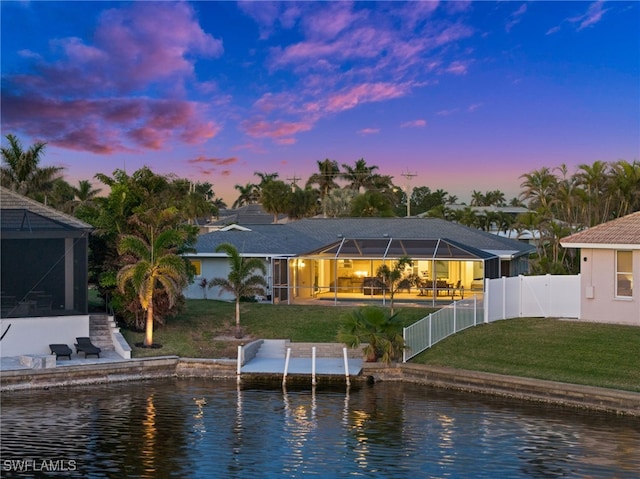 back house at dusk with a water view, a lanai, and a yard