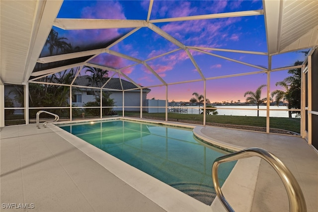 pool at dusk with a lanai, a patio area, and a water view