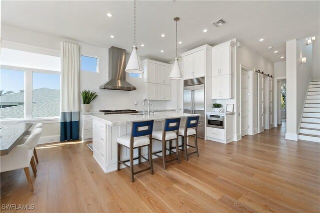 5997 Cypress Ln, Bonita Springs, FL 34134 - kitchen featuring a breakfast bar area, a center island with sink, light wood finished floors, stainless steel appliances, and wall chimney exhaust hood