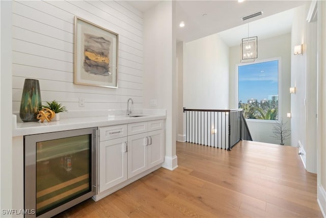 bar featuring wine cooler, sink, white cabinetry, light wood-type flooring, and pendant lighting