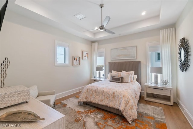 bedroom with ceiling fan, a tray ceiling, and light wood-type flooring