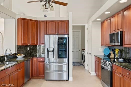 kitchen with sink, dark stone countertops, stainless steel appliances, separate washer and dryer, and decorative backsplash