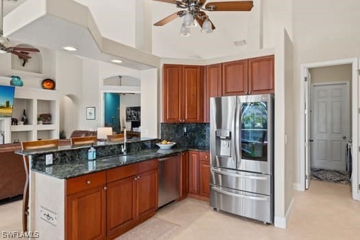 kitchen with appliances with stainless steel finishes, sink, dark stone countertops, ceiling fan, and kitchen peninsula