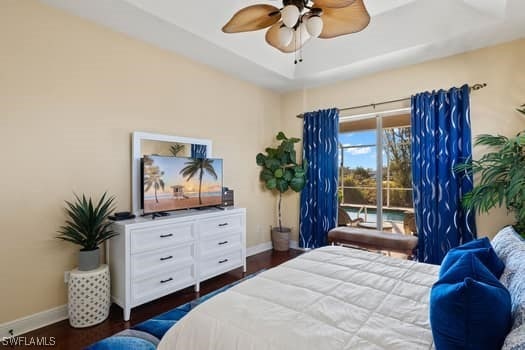 bedroom with ceiling fan, dark hardwood / wood-style flooring, a raised ceiling, and access to outside