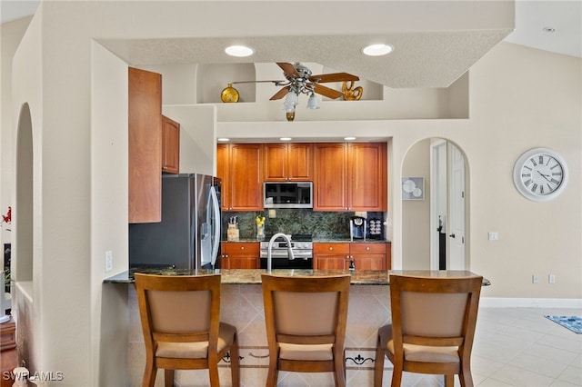 kitchen featuring a breakfast bar, ceiling fan, stainless steel appliances, decorative backsplash, and kitchen peninsula