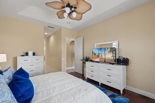 bedroom featuring ceiling fan, dark hardwood / wood-style flooring, and a tray ceiling