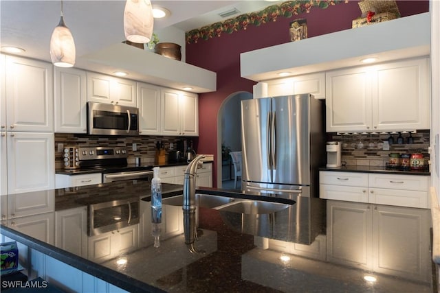 kitchen with stainless steel appliances, dark stone countertops, pendant lighting, and white cabinets