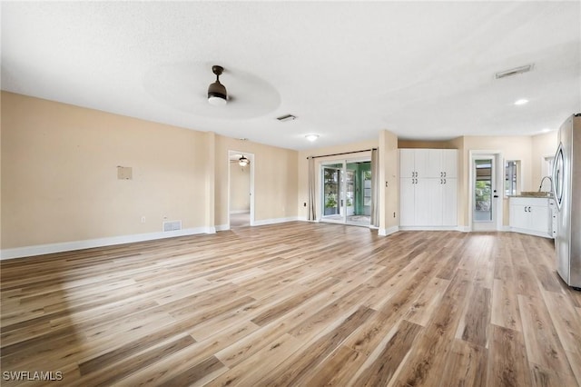 unfurnished living room featuring light wood-style floors, baseboards, visible vents, and a ceiling fan