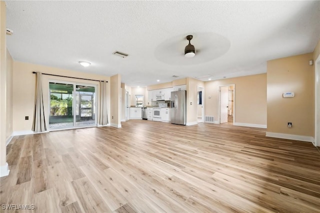 unfurnished living room featuring light wood-style floors, visible vents, ceiling fan, and a textured ceiling