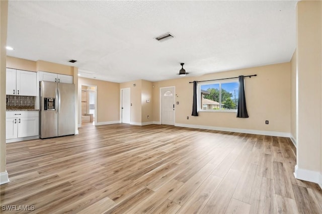 unfurnished living room with light wood finished floors, visible vents, and baseboards