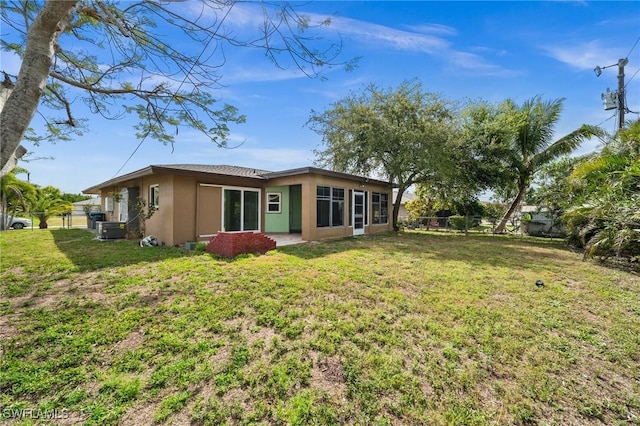 back of property featuring central air condition unit, fence, a lawn, and stucco siding