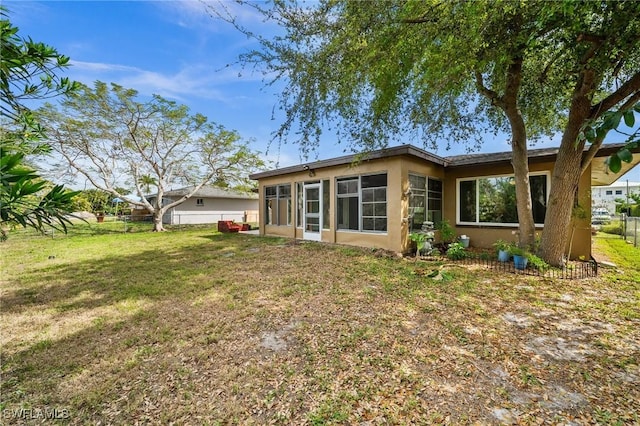 rear view of house with fence, a lawn, and stucco siding