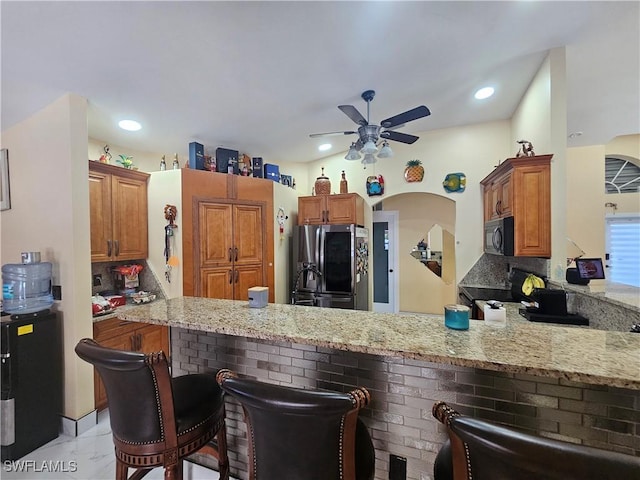 kitchen with light stone counters, kitchen peninsula, stainless steel fridge with ice dispenser, and a breakfast bar area