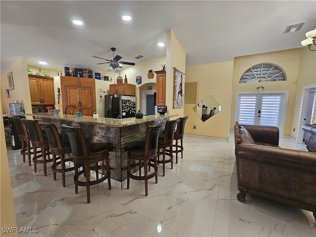 kitchen featuring a kitchen bar, kitchen peninsula, black refrigerator with ice dispenser, and light stone countertops