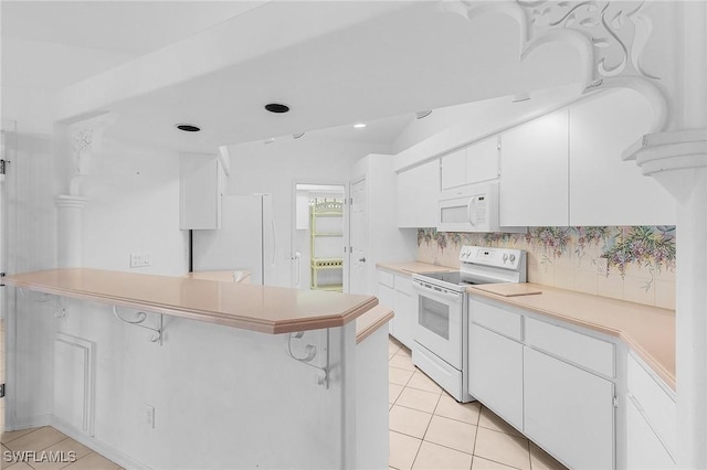 kitchen featuring a breakfast bar, white cabinetry, light tile patterned floors, kitchen peninsula, and white appliances