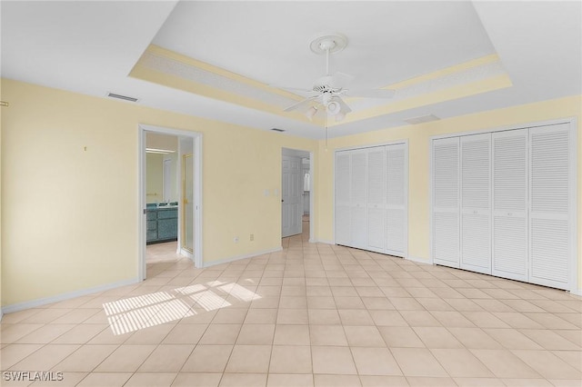 unfurnished bedroom featuring multiple closets, ceiling fan, a raised ceiling, and light tile patterned floors