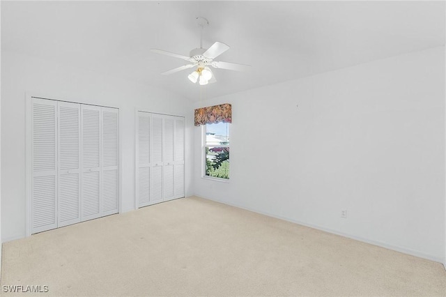 unfurnished bedroom featuring multiple closets, light colored carpet, and ceiling fan