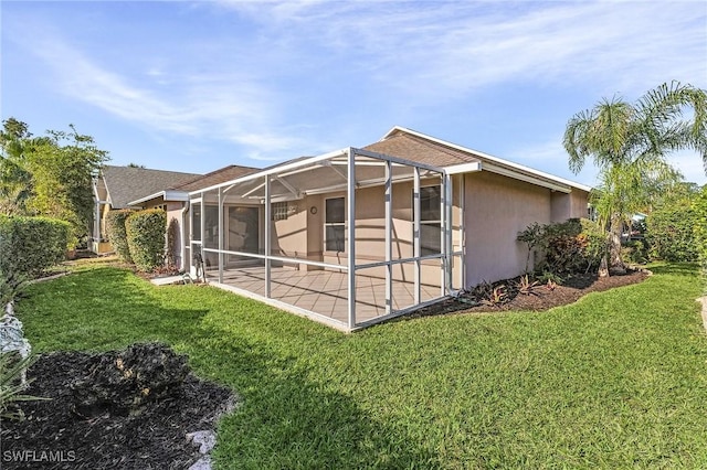 rear view of house with glass enclosure, a yard, a patio area, and stucco siding