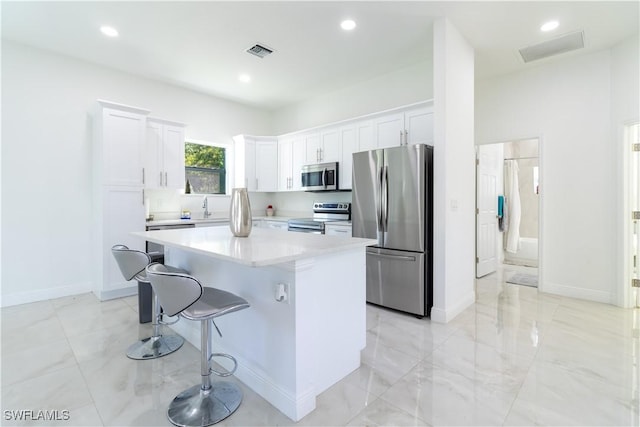 kitchen with sink, stainless steel appliances, a center island, white cabinets, and a kitchen bar