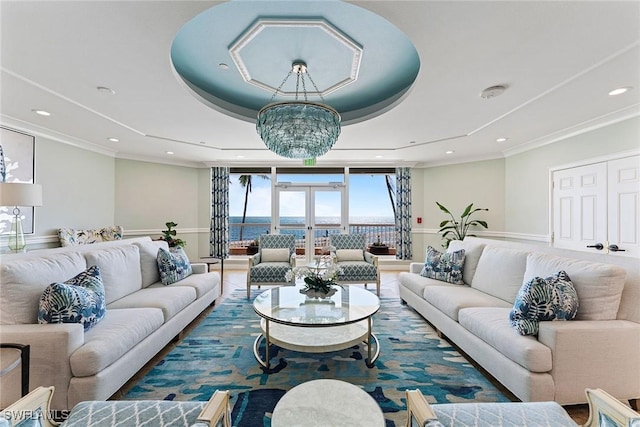 living room with crown molding, a water view, a notable chandelier, and a tray ceiling