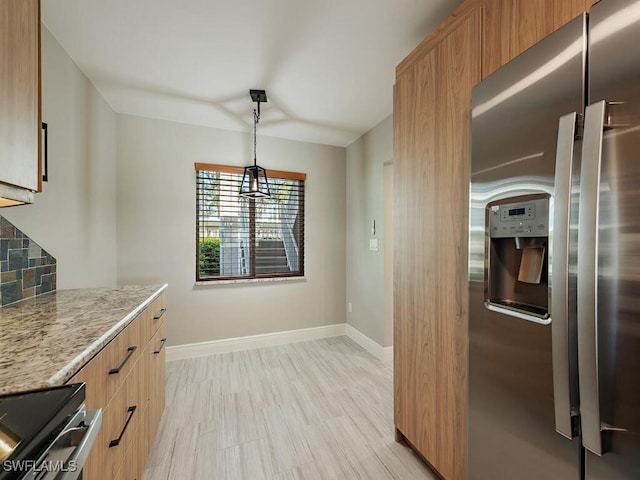 kitchen featuring tasteful backsplash, stainless steel fridge, pendant lighting, light stone countertops, and stove