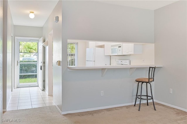 kitchen featuring a breakfast bar, white appliances, light countertops, light tile patterned floors, and light colored carpet