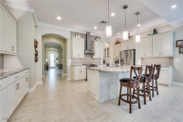 kitchen featuring high end fridge, hanging light fixtures, light stone counters, and wall chimney exhaust hood