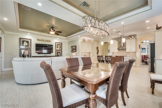 dining area featuring a raised ceiling, ornamental molding, and ceiling fan with notable chandelier