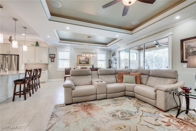 living room featuring light tile patterned flooring, ceiling fan, ornamental molding, and a tray ceiling