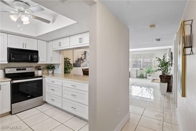 kitchen featuring light tile patterned floors, white cabinetry, tasteful backsplash, a tray ceiling, and stainless steel electric range oven