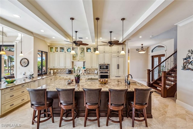 kitchen featuring a kitchen breakfast bar, pendant lighting, stainless steel appliances, light stone countertops, and cream cabinetry