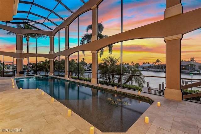 pool at dusk with a patio, a water view, and a lanai