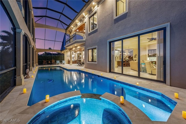 pool at dusk with an in ground hot tub, a patio, and glass enclosure