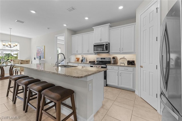 kitchen with white cabinetry, sink, stainless steel appliances, and an island with sink