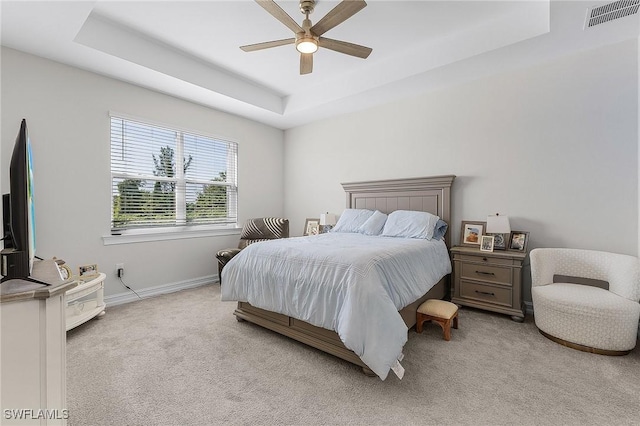 carpeted bedroom with a raised ceiling and ceiling fan