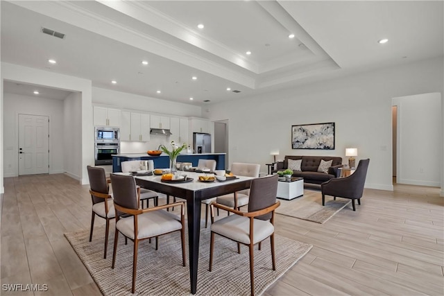 dining space with light hardwood / wood-style flooring, ornamental molding, and a raised ceiling