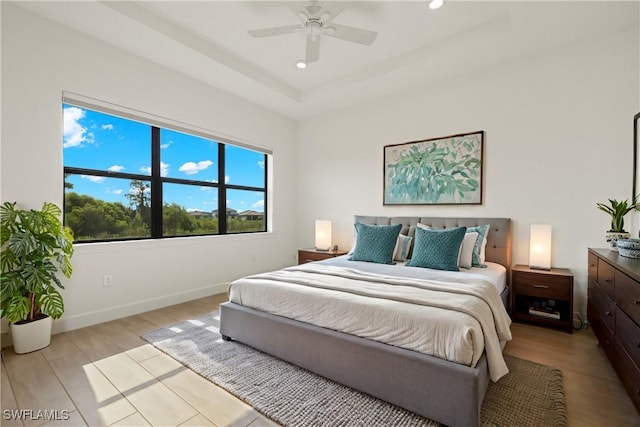 bedroom featuring ceiling fan, a tray ceiling, and light wood-type flooring