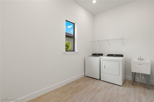 clothes washing area featuring sink, washing machine and dryer, and light hardwood / wood-style flooring