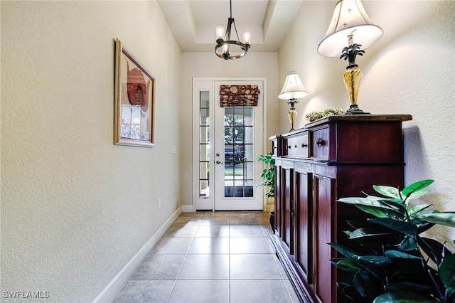 doorway to outside with light tile patterned floors, an inviting chandelier, and a tray ceiling